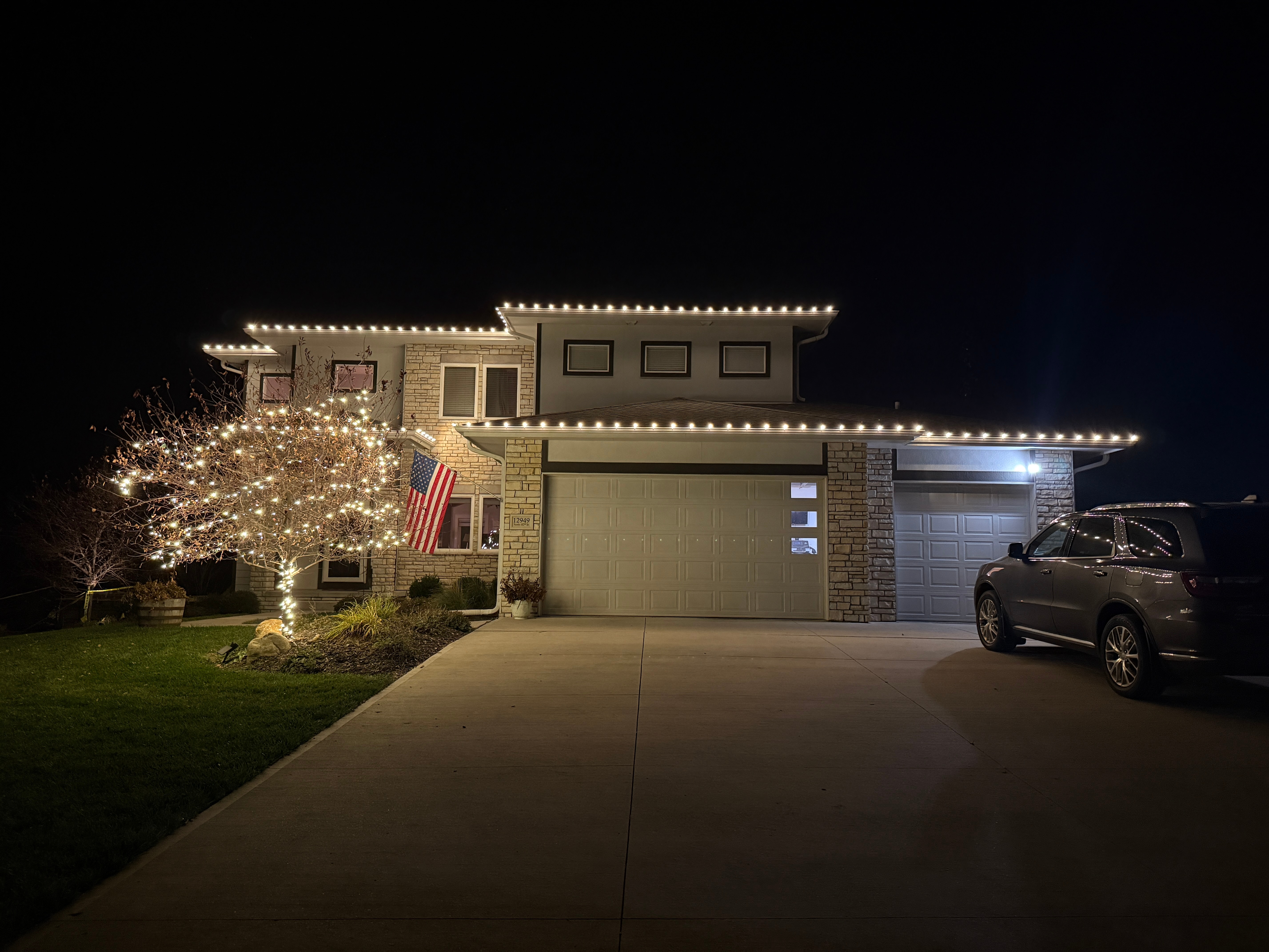 Home with a warm-white roofline outline and a fully light-wrapped front-yard tree