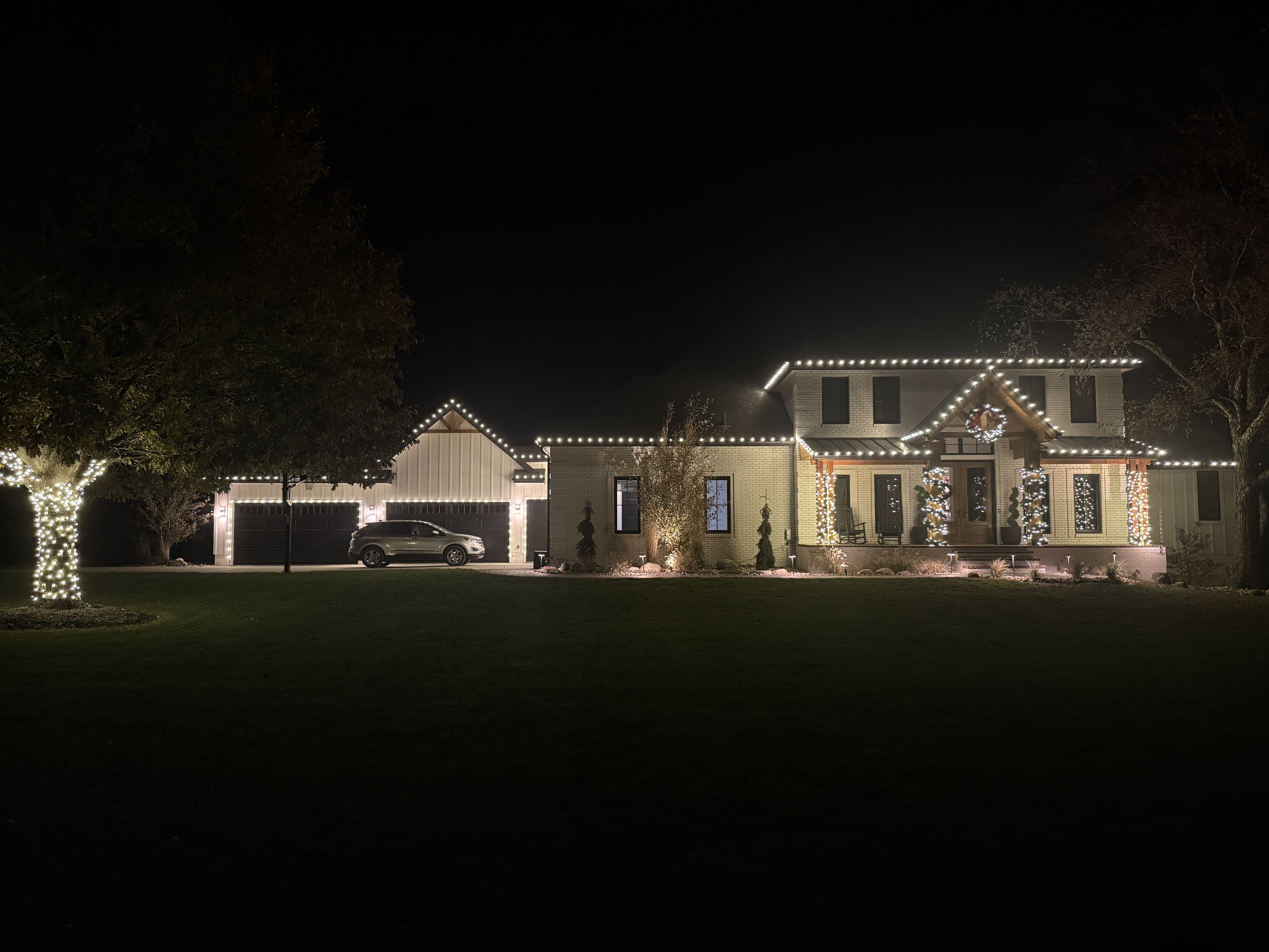 White-brick home with a clean warm-white roofline outline and a lit front-door wreath